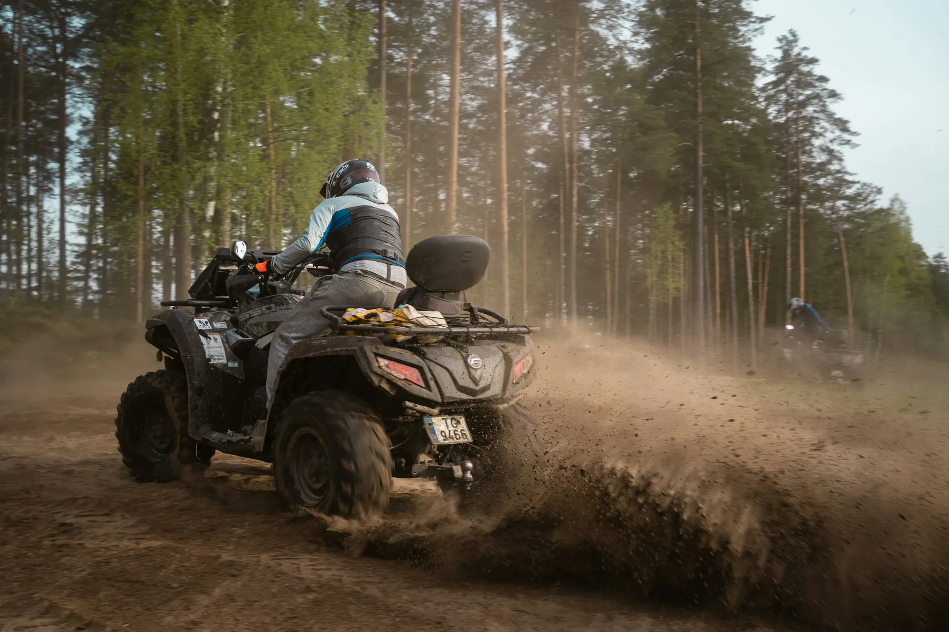 A person riding a quad and kicking up dust